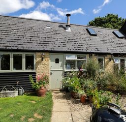 Exterior of a stone and wood house with a front door windows potted plants and a charcoal grill at Henmarsh Cottage in Moreton-In-Marsh