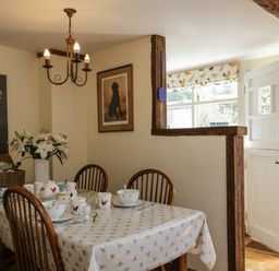 A dining area with a table set with cups bowls and plates and wooden chairs near an open door at Henmarsh Cottage in Moreton-In-Marsh
