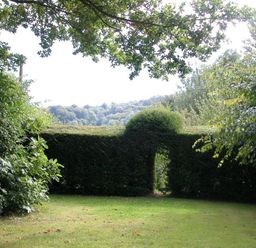 A garden with a grass lawn and a hedge with an arched opening surrounded by trees at The Yeomans House in Bignor