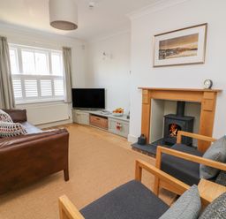 A living room with a brown leather sofa two grey armchairs a wood burning stove television and a window with curtains at Craigluscar in Newport Pembrokeshire