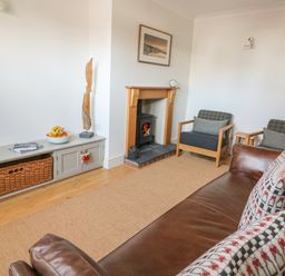 A living room with a brown leather sofa and patterned cushions two armchairs a wooden fireplace and a TV cabinet with a basket and bowl of fruit at Craigluscar in Newport Pembrokeshire