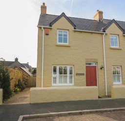 A yellow stone house with a red door and white windows at Craigluscar in Newport Pembrokeshire