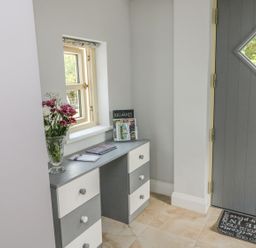 An entryway with a gray door with a diamond window a small table with drawers flowers books and brochures on it at Dromstabla in Glencar