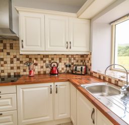 A kitchen with white cabinets wooden countertops a stainless steel sink a window and appliances at Dromstabla in Glencar