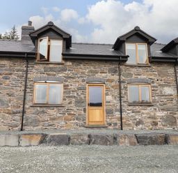 Stone exterior wall with wooden door and windows under a cloudy sky at Llety Dewi in Lake Vyrnwy