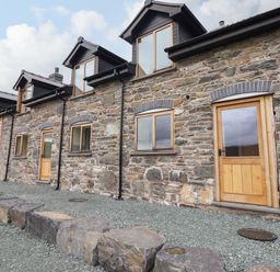Stone house exterior with wooden doors and windows and gravel ground at Llety Dewi in Lake Vyrnwy