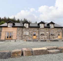 A stone house with four dormer windows and wooden doors surrounded by gravel and trees at Old Cart House in Llanwddyn