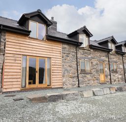 The exterior of a stone and wood house with multiple windows and wooden doors at Old Cart House in Llanwddyn