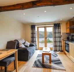 A living area with a gray sofa wooden dining table chairs and a kitchen with wooden cabinets and appliances at Old Cart House in Llanwddyn