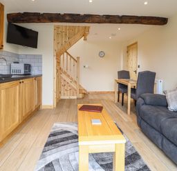 A kitchen and living area with wooden cabinets a grey sofa a wooden table with two chairs and a staircase at Old Cart House in Llanwddyn