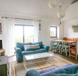 A living room with two blue sofas a glass coffee table a wood burning stove and a dining area with wooden bench and chairs at The Schooner in Goleen County Cork