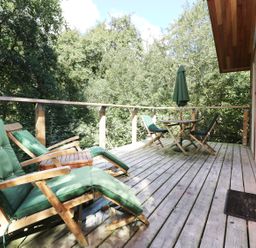 A wooden deck with green cushioned chairs a table with umbrella and surrounded by trees at 6 Streamside in Lanreath