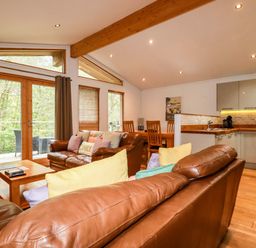 A living room with brown leather sofas a wooden coffee table a dining table and a kitchen area at 6 Streamside in Lanreath