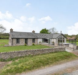 A stone cottage with a slate roof and a fenced garden in a rural setting at Hen Hafod in Talwrn near Llangefni