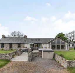 A stone and white exterior house with a paved patio outdoor furniture and grass at Hen Hafod in Talwrn near Llangefni