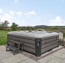 An outdoor hot tub with water jets on a stone patio with green fields and hills in the background at Hen Hafod in Talwrn near Llangefni