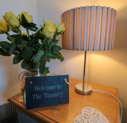A wooden table with a vase of yellow roses a table lamp and a welcome sign at The Tannery in Whitby