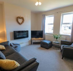 A living room with two windows a wall-mounted fireplace a television on a wooden stand and leather seating at The Tannery in Whitby