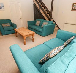 A living room with teal sofas a wooden coffee table stairs and paintings on walls at The Chace in Portreath