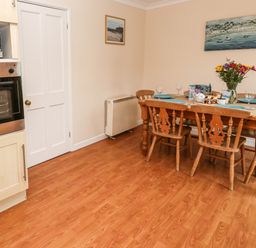 A dining area with a wooden table set with plates and glasses next to a built-in oven and microwave at The Chace in Portreath