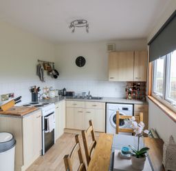 A kitchen with wooden cabinets a dining table and a window with a blind at Kestrel Lodge in Dumfries