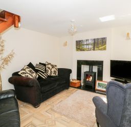 A living room with sofas a fireplace a television and a wooden staircase at Rose Cottage in Bream