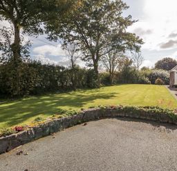 A garden with trees grass and a stone wall next to a stone house at Llain Bach in Llangefni