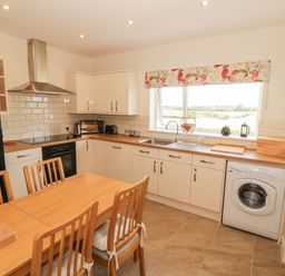 A kitchen with wooden dining table and chairs a washing machine black refrigerator and window with floral valance at Llain Bach in Llangefni