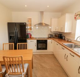 A kitchen with wooden dining table and chairs black refrigerator white cabinets and countertops with sink at Llain Bach in Llangefni