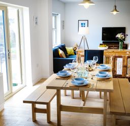 A dining area with a wooden table set with blue bowls and glasses at Oystercatcher in Embleton