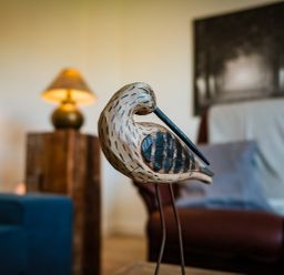 A wooden bird sculpture on a table with a lamp a chair and a wall painting in the background at Oystercatcher in Embleton