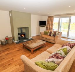 A living room with two sofas and a wooden coffee table near a fireplace and sliding glass doors at Rhos Y Foel Cottage in Nefyn