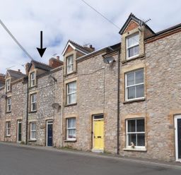 A row of stone terraced houses with various colored doors along a street with an arrow pointing to one house at Anchorage Watchet
