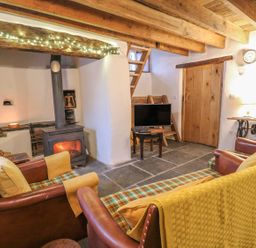 A living room with leather armchairs a wood burning stove TV and a wooden door at Bwthyn Lan in Boncath