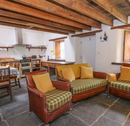 A kitchen and living area with wooden beams on the ceiling a table with chairs and leather armchairs at Bwthyn Lan in Boncath