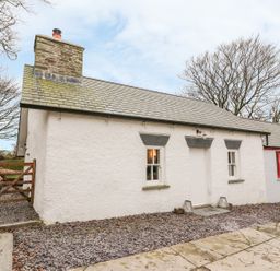 An exterior view of a white cottage with a slate roof a stone chimney two windows and a wooden gate at Bwthyn Lan in Boncath