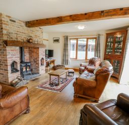 A living room with leather armchairs a wooden coffee table a brick fireplace and a wooden cabinet at Pentrego Isaf in Meifod