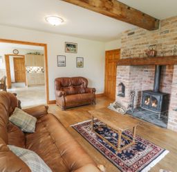 A living room with brown leather sofas wood flooring a wooden coffee table a rug and a brick fireplace with a wood stove at Pentrego Isaf in Meifod