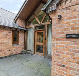 An exterior brick entrance with a wooden door and large windows at Pentrego Isaf in Meifod