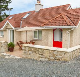 A house with a red tiled roof and a red door with a stone wall and outdoor table with chairs and umbrella at Cnoc suan in Aughavas County Leitrim
