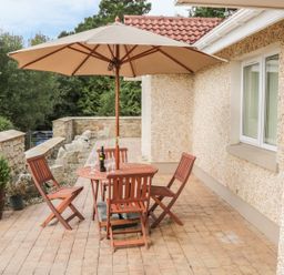 An outdoor patio area with a wooden table and chairs under a large beige umbrella surrounded by stone walls and greenery at Cnoc suan in Aughavas County Leitrim