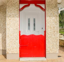 A red wooden gate in front of a white door with glass panels on a speckled exterior wall at Cnoc suan in Aughavas County Leitrim
