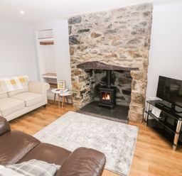 A living room with a stone fireplace a wood burning stove two sofas a TV on a stand and two side tables at 3 Green Terrace in Llangaffo near Newborough