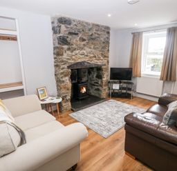 A living room with two sofas a stone fireplace and a television at 3 Green Terrace in Llangaffo near Newborough