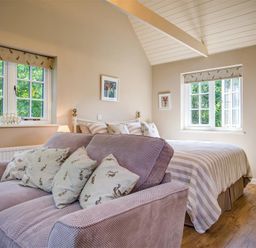 A bedroom with a bed and a sofa with cushions near two windows at Lime Tree in Burford