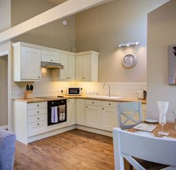 A kitchen with white cabinets wooden countertops a dining table with chairs and a rabbit painting on the wall at Lime Tree in Burford