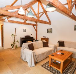 A living room with exposed wooden beams two sofas covered with fabric a wooden coffee table and a piano at Honey Buzzard Barn in Fakenham