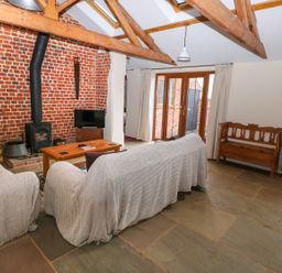 A living room with two covered sofas wooden coffee table wood stove under exposed beams at Honey Buzzard Barn in Fakenham