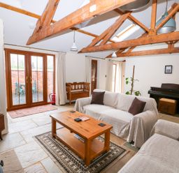 A living room with wooden beams two sofas a wooden coffee table a piano and a TV at Honey Buzzard Barn in Fakenham