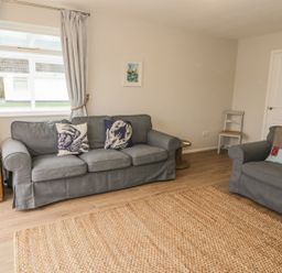 A living room with gray sofas and a woven rug at Ty Taid in Rhosneigr